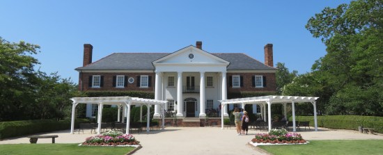 Two-story Colonial Revival manor with four white columns and two sheltered sections of chairs out front, as if for an upcoming wedding.