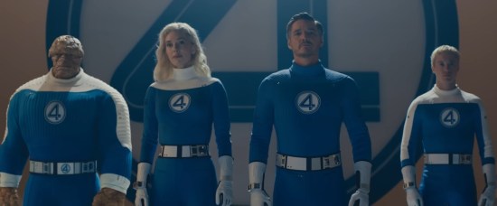 Fantastic Four cast in movie costumes, just standing and staring. Big blue 4 logo takes up the wall behind them.