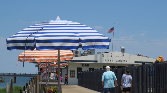 Fleet Landing restaurant with large fence between it and several patio tables with blue and orange umbrellas.