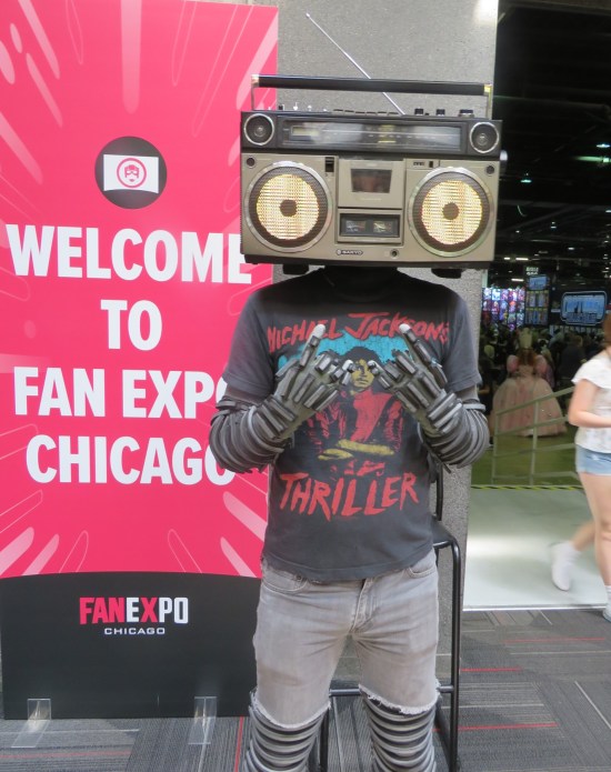 Guy with boombox on head, speakers turned into eyes that could blink, wearing a Thriller T-shirt and standing next to a "Welcome to Fan Expo Chicago" sign.