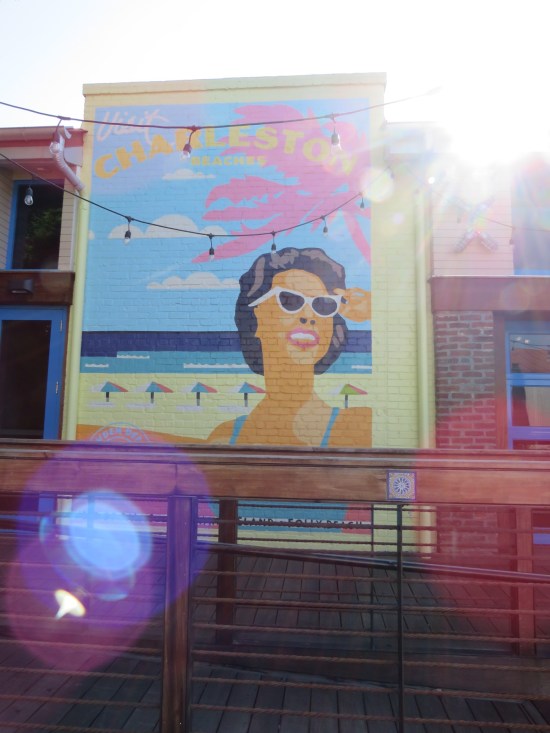 Colorful vertical mural reading "Visit Charleston Beaches" with pastel images of woman with sunglasses on sunny beach.