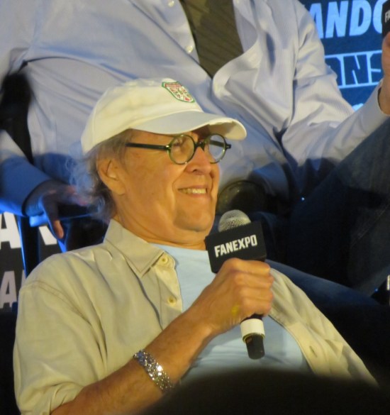 Chevy Chase on stage, smiling with mic in hand.