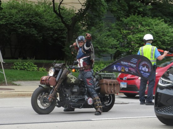 Captain America cosplayer on an actual motorcycle, in stopped traffic and holding Mjolnir in one hand.