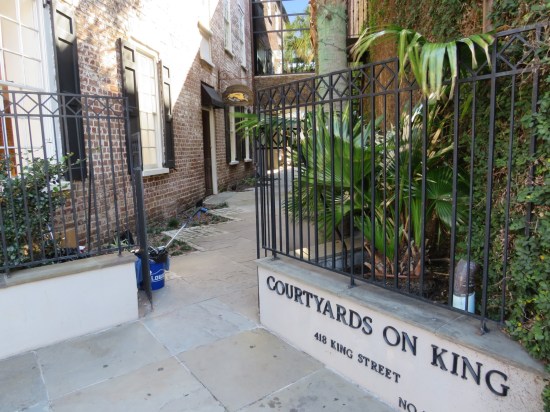 Alley between two brick buildings with black metal fences on either side of its ungated entrance. 