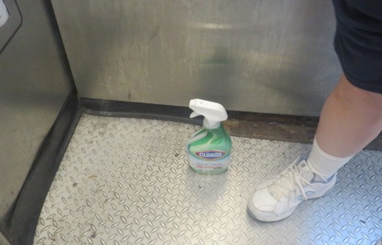 Elevator with metal-lined floor and wall. Anne's white sneaker rests next to a half-empty squirt bottle of Clorox.