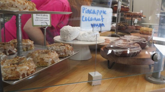 Donut shop front counter with donuts in various displays. Names on signs include "Pineapple coconut lemon" and "Black and White", which we'll get to in a moment.