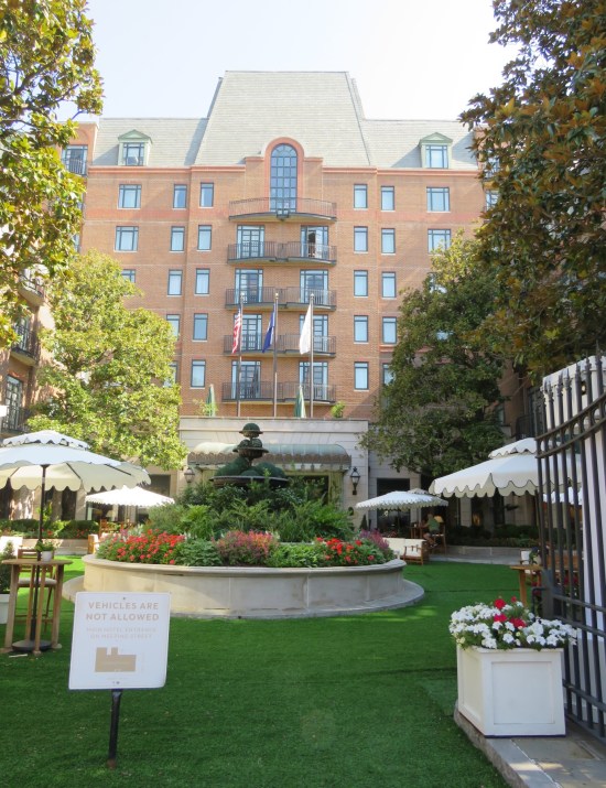 tall tiered fountain in a fake grassy promenade in front of a 7-story brick hotel.