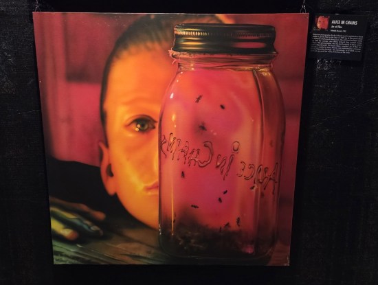 Red-filtered photo of tiny child sticking his head on a table to stare at a jar of flies.