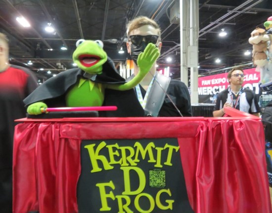 Puppeteer carrying a red-clothed table with a Kermit puppet on top, dressed like a stage magician.