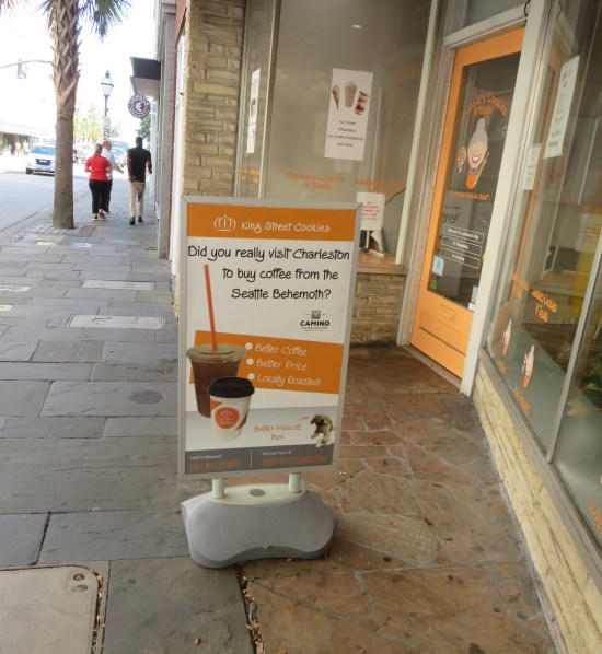 Sign outside orange-colored King Street Cookies reads "Did you really visit Charleston to buy coffee from the Seattle behemoth?"