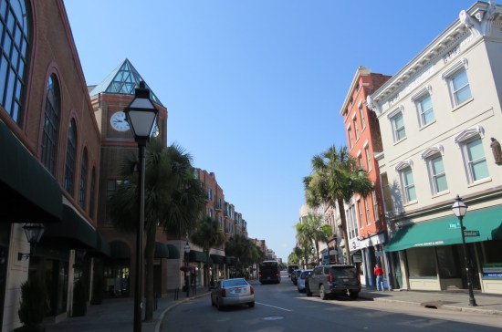 curving street with stores and palmettos on either side. At the bend is a tall clock tower.