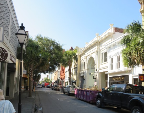 Dense city street packed with businesses on both sides that keep changing colors and architectural styles. Signs include Chipotle and Mudhouse.