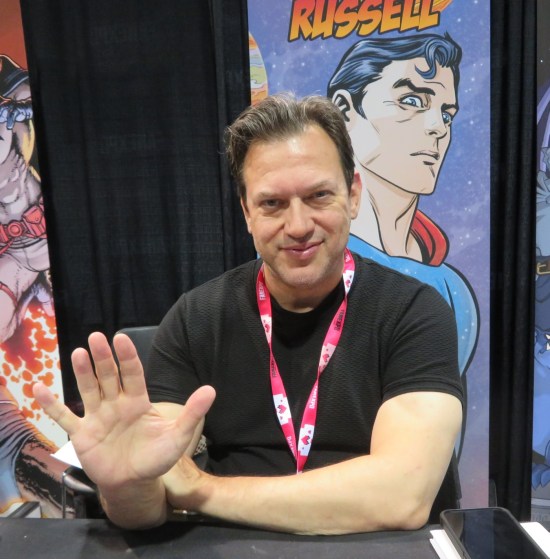 Mark Russell waving from his booth. His banner has Michael Allred art from Superman: The Space Age.