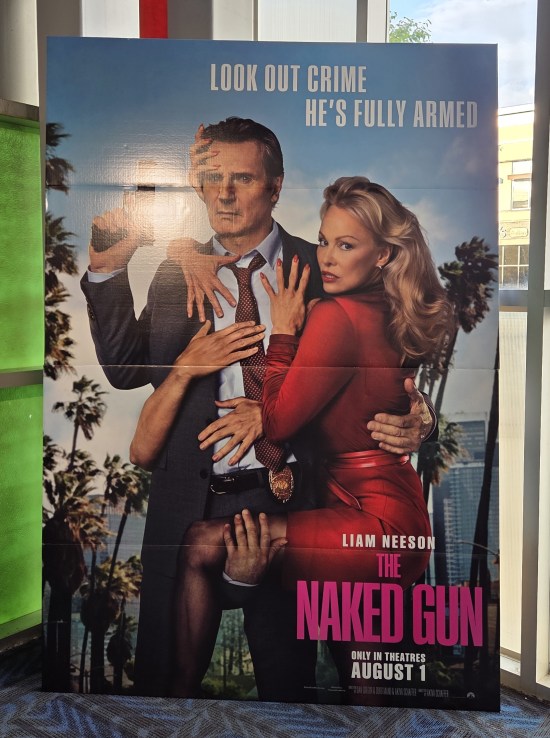 Theater lobby standee with Liam Neeson in character groping at Pamela Anderson with five different hands while brandishing his gun with a sixth.
