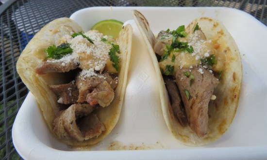 Two tiny tacos with strips of thin-sliced steak and herbed cheese sauce on top.
