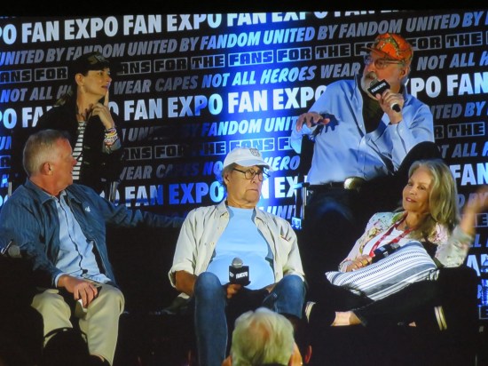 Photo of large screen showing five vacation actors. Chase is in the middle and seems to have a big spotlight aimed at him from above.