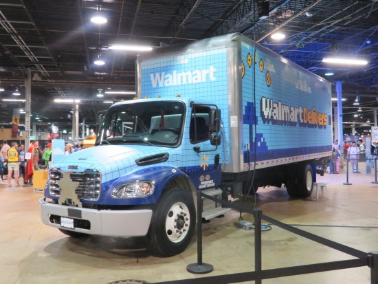 Walmart truck parks in the middle of a convention center. Blue and with art on the side in 8-bit art reading "Walmart Delivers".