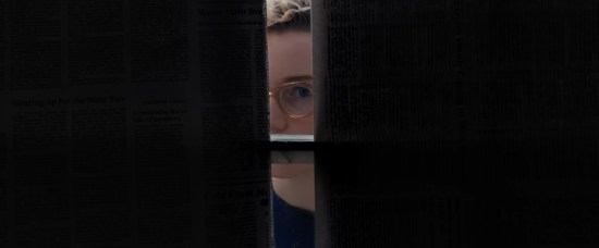 Julia Garner peeking through open curtains from outside into a darkened house.
