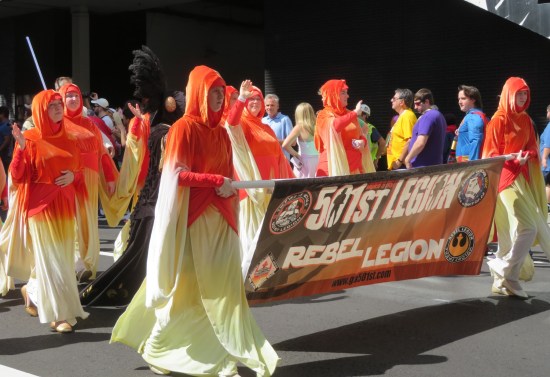 Several 501st Handmaiden cosplayers marching with their two groups' joint banner.