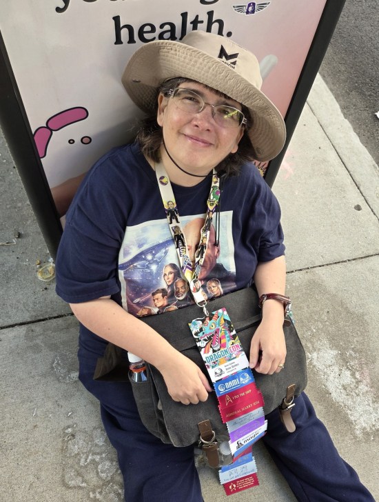 Anne in hat sitting against a trash can, smiling up at me.