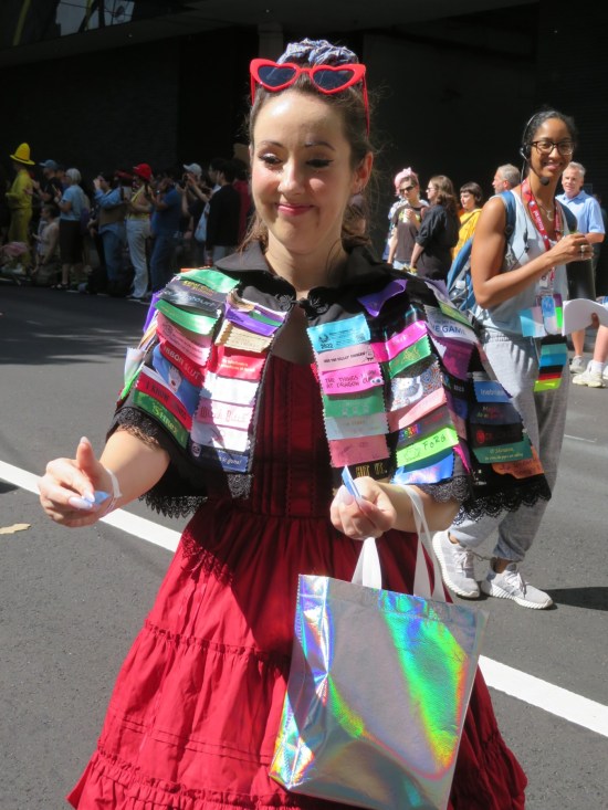 Woman with strands of dozens of comic-con badge ribbons hanging from her red dress.