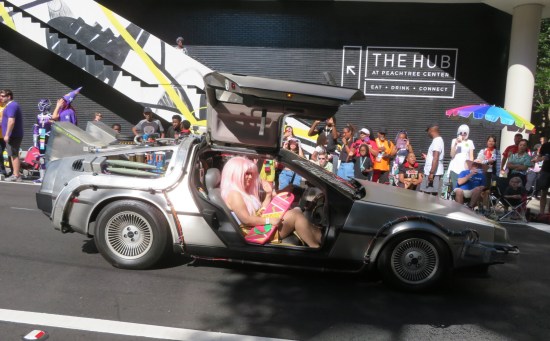 Woman with pink hair and hoverboard riding in a DeLorean with the doors open.