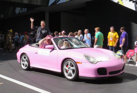 Brian Brushwood riding in the back of a pink convertible with pink graduates riding in the front seats.