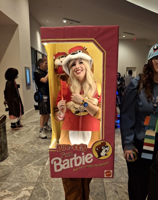 Barbie costume walking around inside a big pink box with Buc-ee mascot drawn on box, and two plush dolls inside with her.