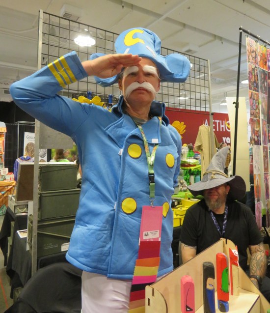 Cap'n Crunch cosplayer, saluting at his dealer table.