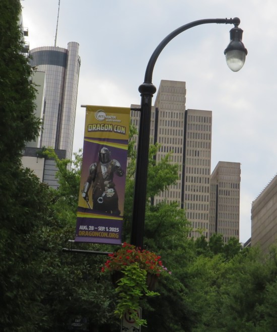 Dragon Con street banner with The Mandalorian on it. Behind it are Atlanta skyscrapers and trees.