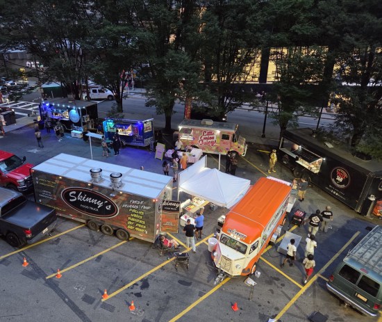Six food trucks in a ring in a parking lot, viewed from two stories above.