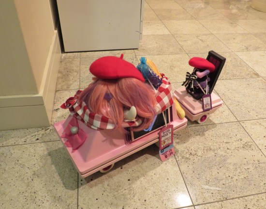 Pink Star Wars mouse droid with a red beret and other random accessories on top, pulling a tiny pink trailer.