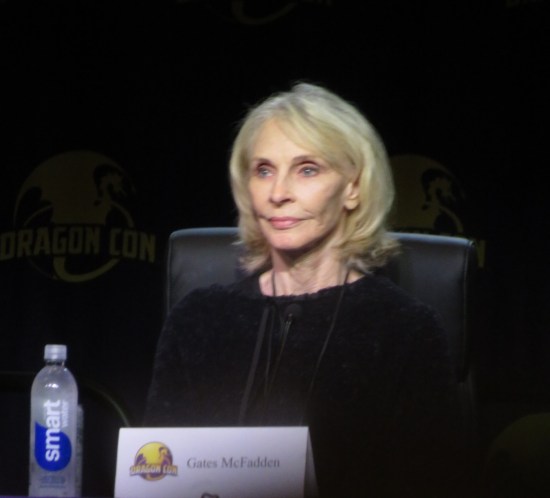 Gates McFadden politely smiling at panel.