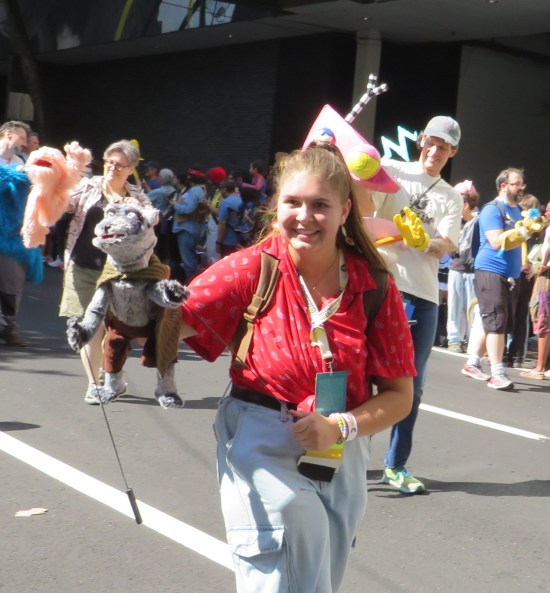 Happy young lady holding a gray rat puppet with brown pants and cape.