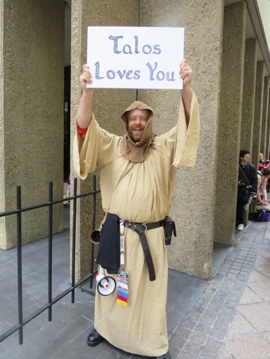 Heimskr costume is brown hooded robe and sign reading "Talos loves you!"