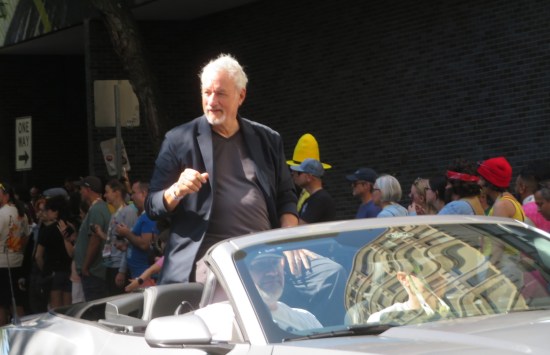 John de Lancie riding in the back of a convertible.