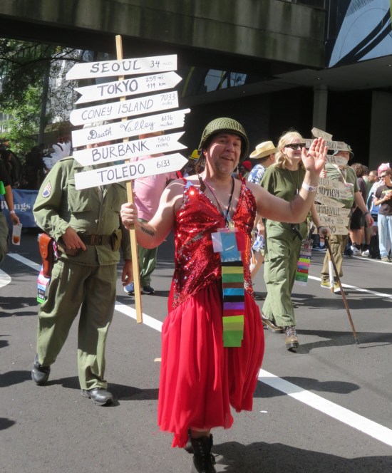 Klinger from MASH cosplayer with road sign bearing arrows to six different cities.
