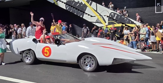 Mach 5 replica with Speed Racer cosplayers waving.