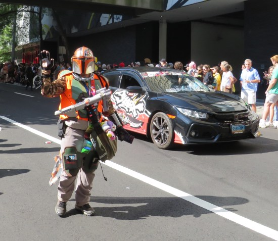 Orange and green Mandalorian cosplayer with space rifle slung from neck