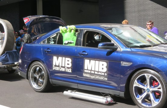 Blue sedan with Men in Black 3 logo on the door and a stuffed green alien sticking out the back window.