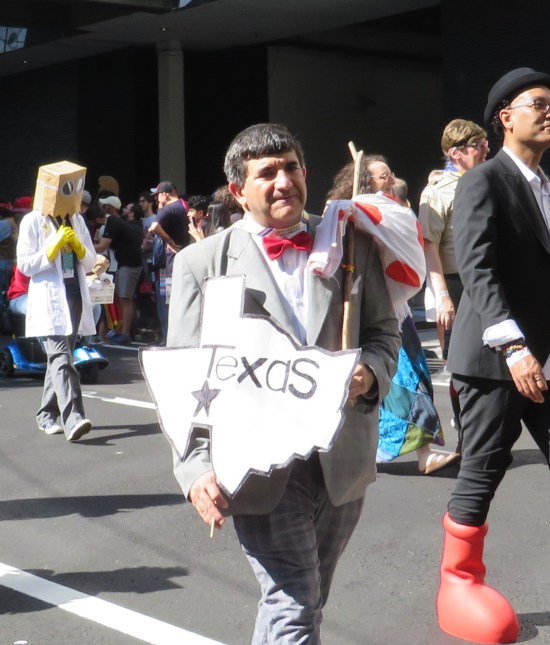Pee-Wee Herman cosplayer holding a hand-drawn Texas sign and a hobo bindle.