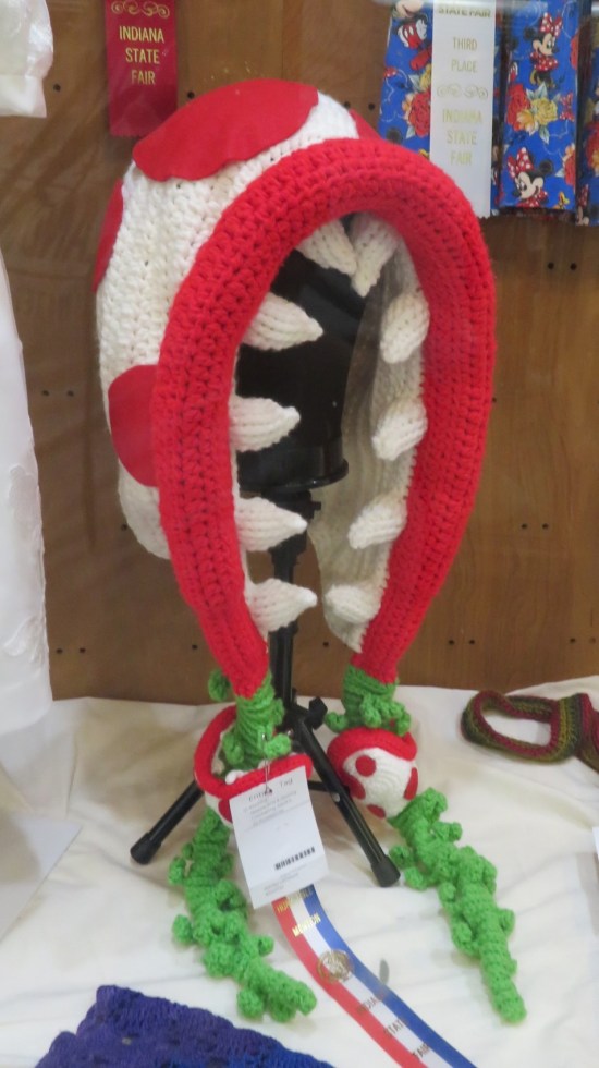 A knitted hood that looks like a red and white piranha plant, lined with plush teeth.