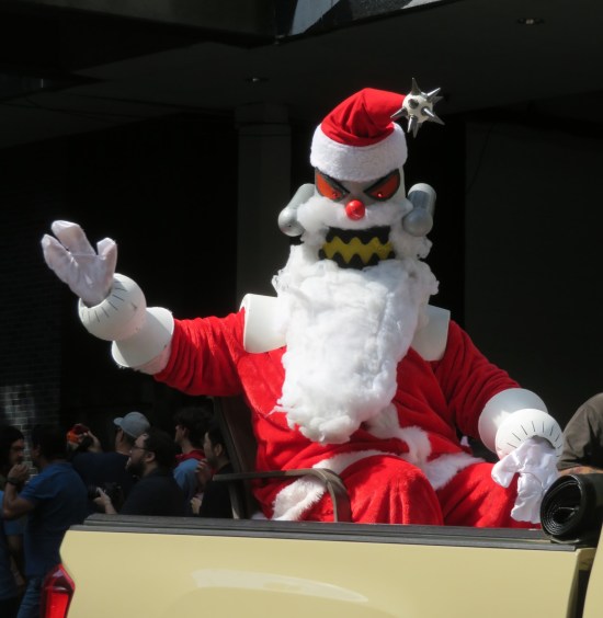 Robot Santa cosplayer waving from the back of a Planet Express pickup truck.
