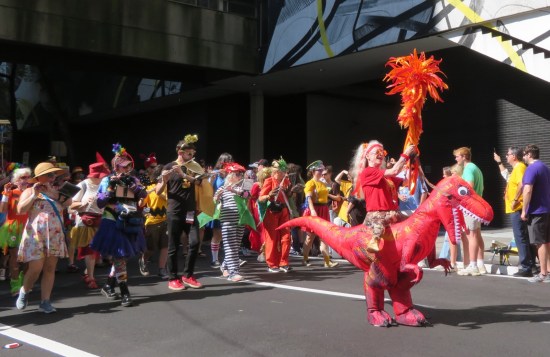 marching band of cosplayers whose leader wears an inflatable red raptor.