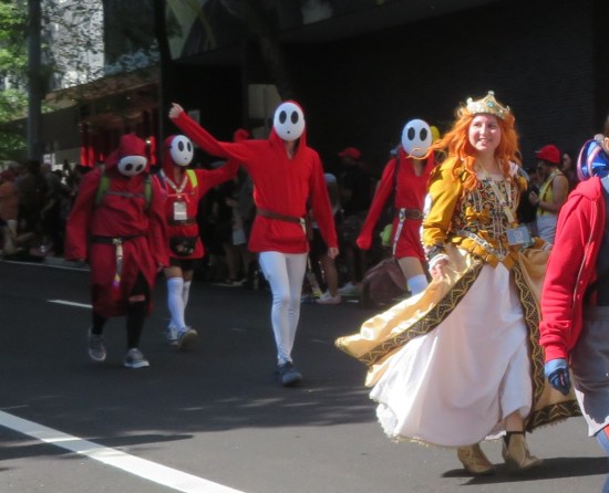 Several Shyguys marching behind a redheaded woman in a ballgown.