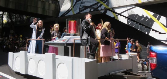 parade float with fake TARDIS control deck. Costumed riders include the Ninth and Thirteenth Doctors and Rose Tyler.