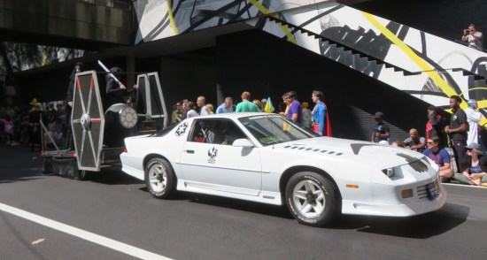 White car with Star Wars decals towing a TIE Fighter on a trailer.