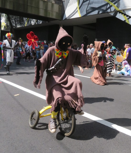 Jawa sitting on tricycle handlebars and pedaling through streets.