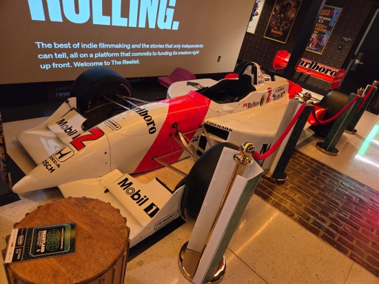 Red and white race car parked in a theater lobby. Decals include Marlboro, Honda, and Mobil.