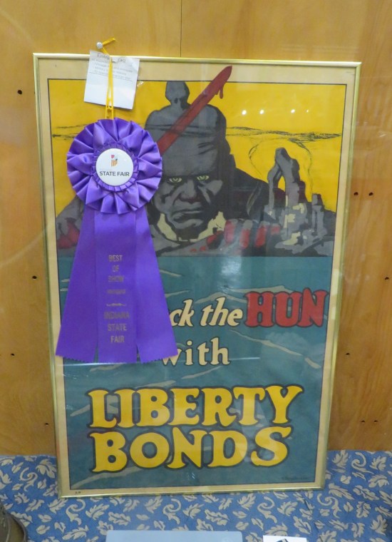 Old poster with gray evil soldier, yellow sky and blue field. Caption: "Beat Back the Hun with Liberty Bonds".